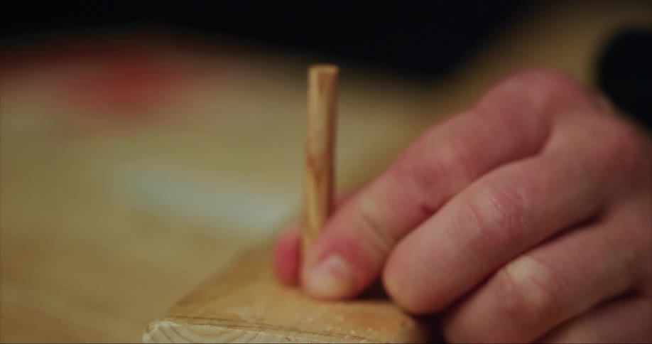 A person hammering a dowel into a piece of wood for a home built sea kayak