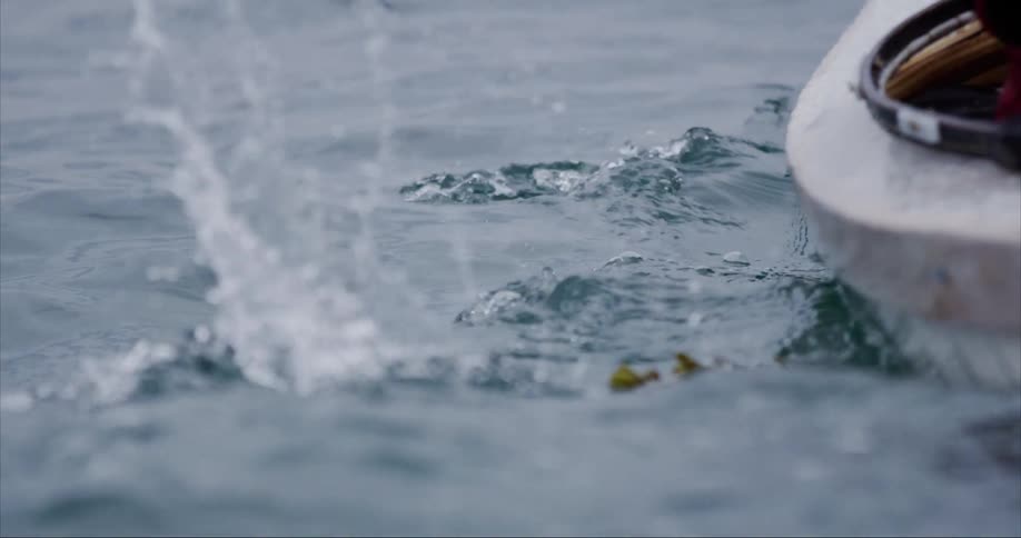 This person paddles their traditional sea kayak in arctic sea water as the paddle rises up out of the water