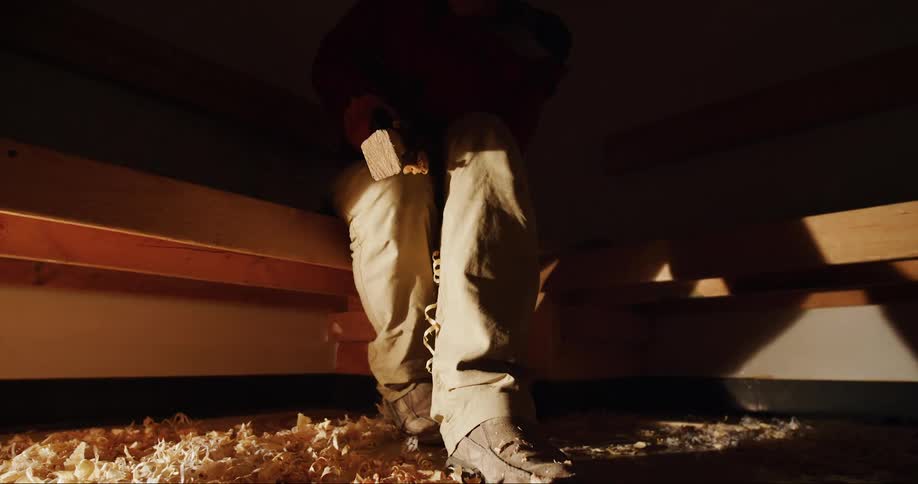 A carpenter shaving a piece of wood with a tool while he builds his sea kayak