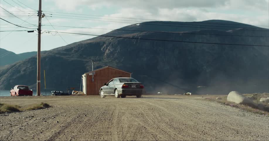 A car is seeing driving up to and then turning a corner on a dirt road near the arctic circle