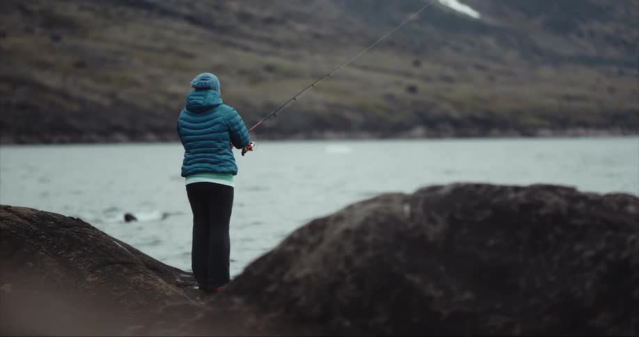 A woman fishing in the ocean on a cold day