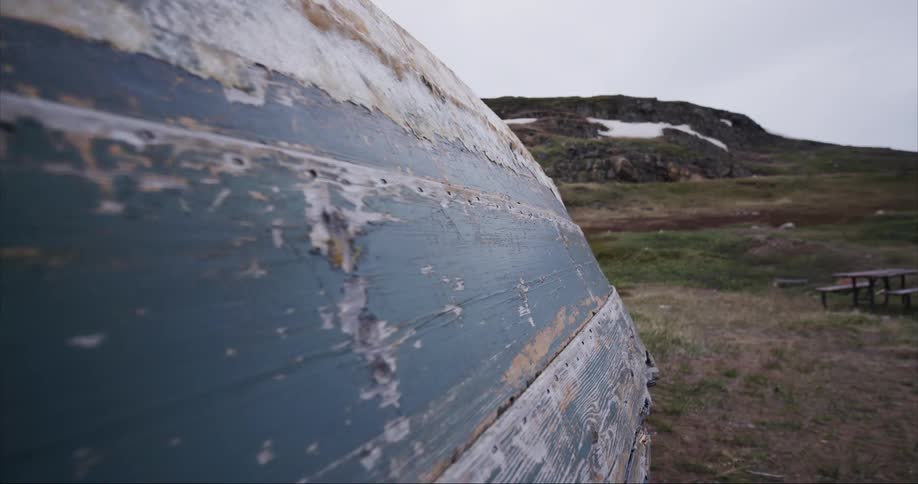 Layers of paint and ice are caked on a overturned fishing boat on Baffin Island on a stormy day