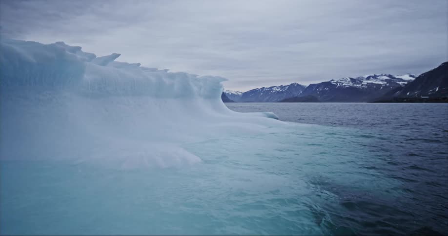 Sea water splashing around the base of an iceberg on a cloudy day in the arctic circle