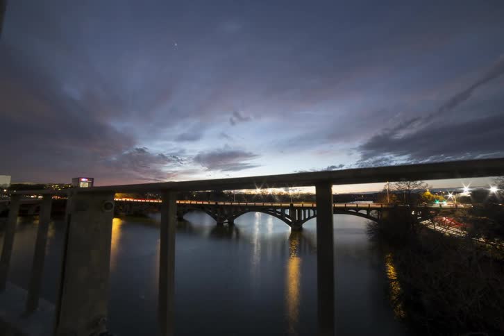 Vehicles pass over a canal bridge and boats travel under in the evening