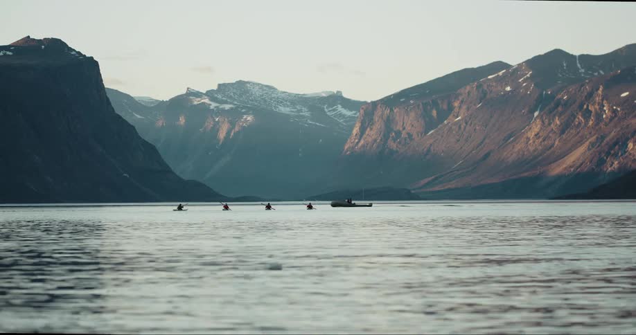 Four adventurers paddle sea kayaks in the Arctic Ocean with beautiful towering granite peaks and glaciers in the background