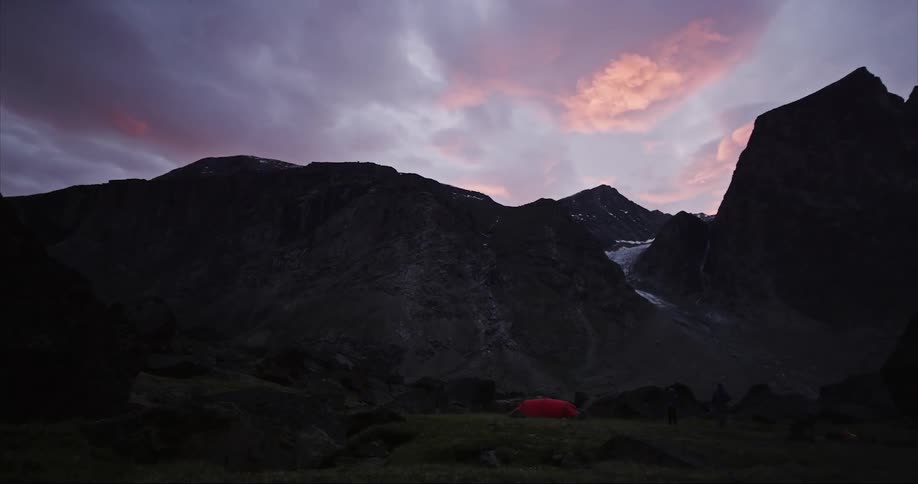 Slow pan of a glacial valley under the midnight sun below towering granite peaks and crags