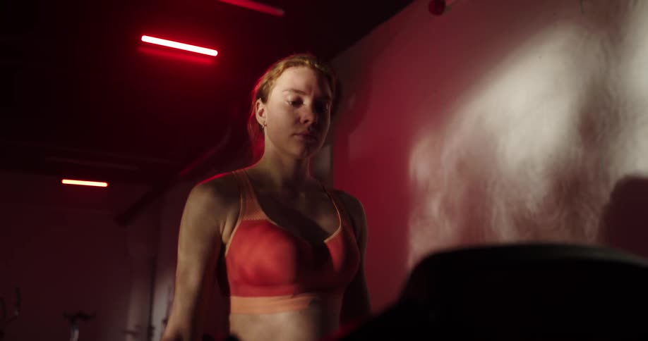 Woman with ponytail and red sports bra walks on treadmill in the gym