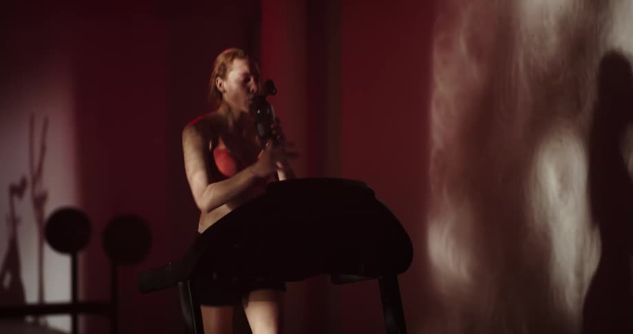 Woman running on treadmill and casting a shadow on wall takes a drink from a water bottle