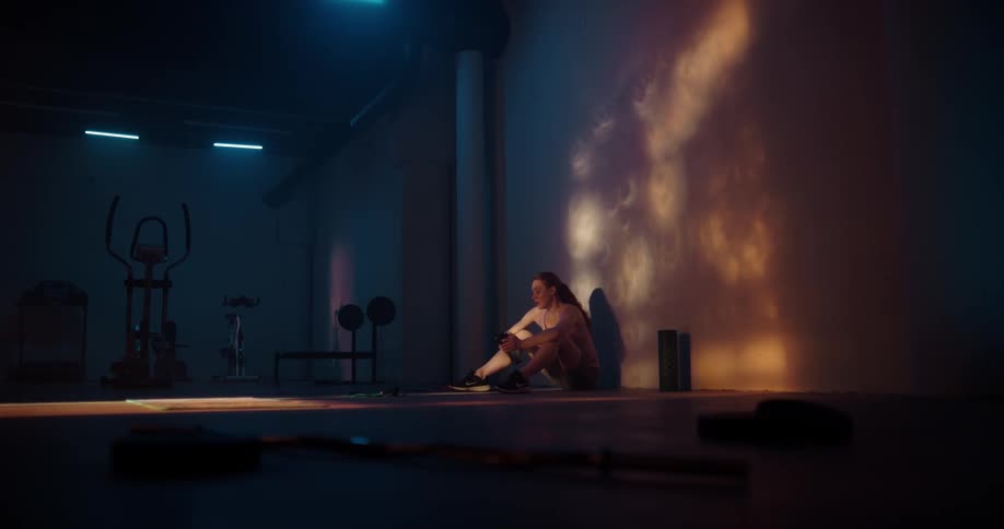 A woman is resting and sitting down in a gym