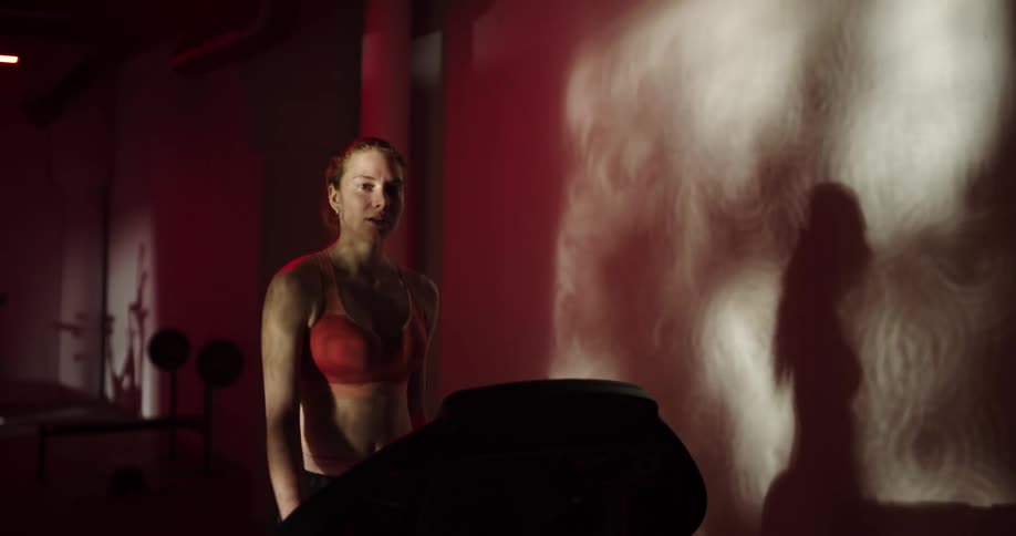 Woman with black shorts and red sports bra exercises on treadmill in the gym
