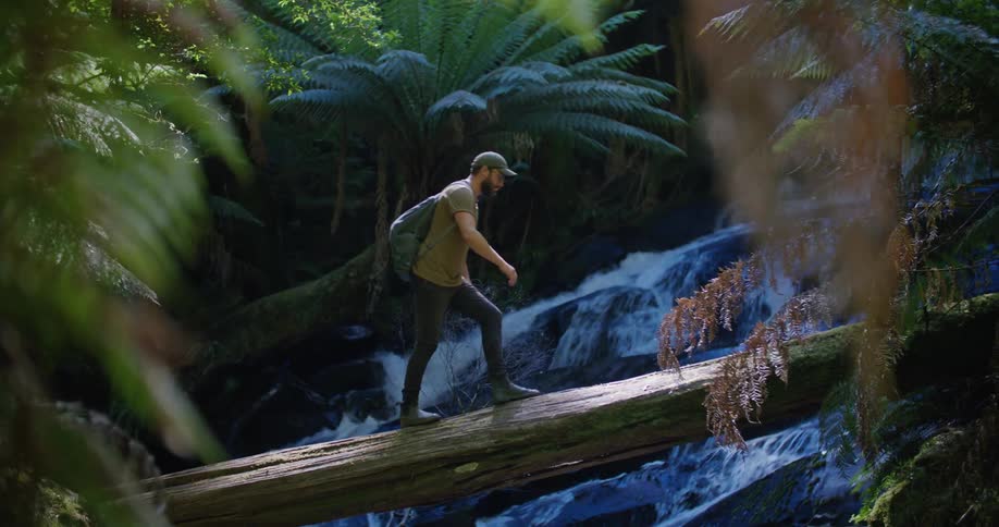 A man jumps onto and walks across a log over a river