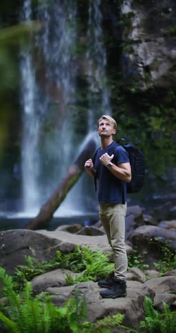 Hiker stands on boulders near pool at bottom of waterfall