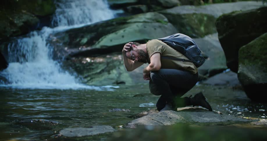 A man cooling off his head with river water while hiking in nature