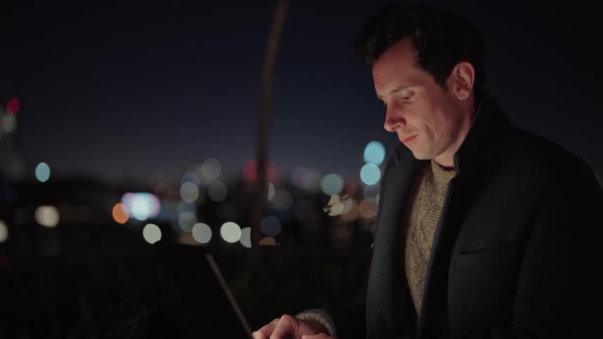 A man works on his laptop while sitting on a city rooftop