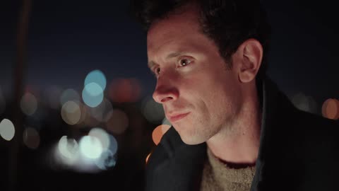 Man in black coat and brown sweater uses laptop typing and thinking at night