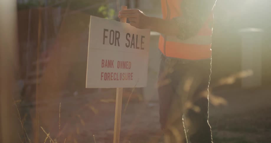 A man hammers in a for sale sign outside a foreclosed property