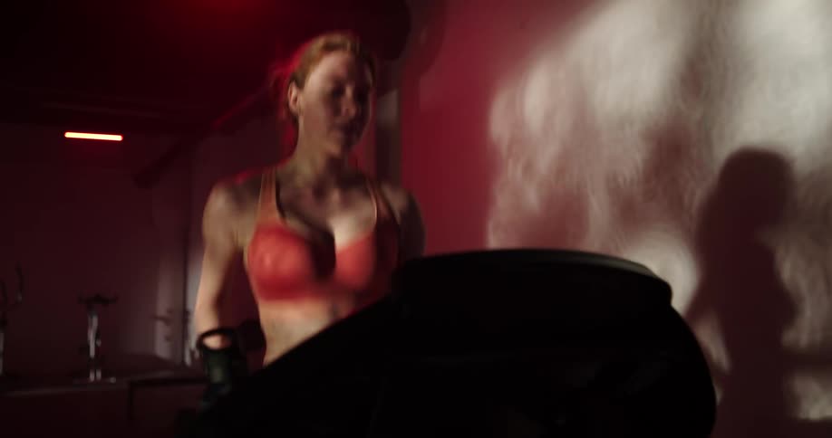 A woman runs on a treadmill in a dimly lit gym during the day