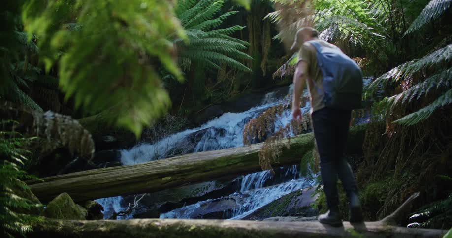 A man walks across a log to cross over a waterfall