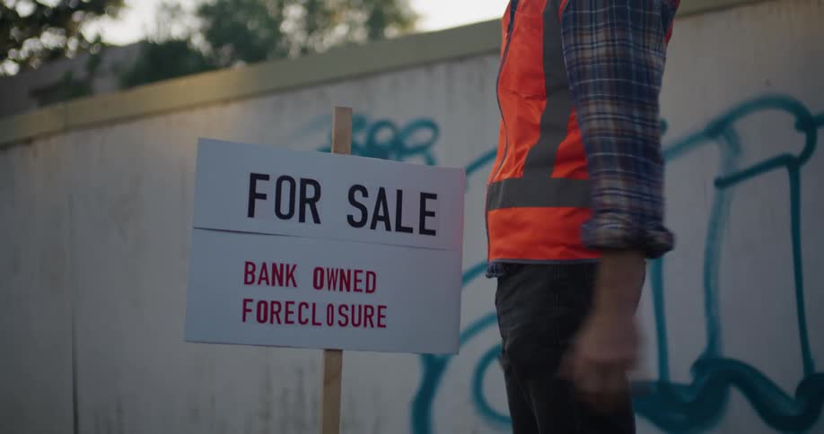A male construction worker hammering a for sale sign in front of a property