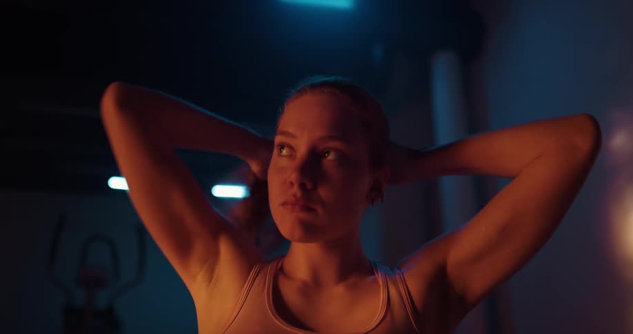 Woman in dimly lit gym puts her hair up into a pony tail