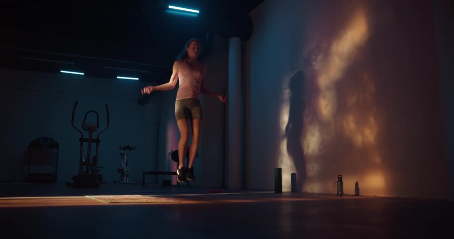 A woman in a home gym picks up a jump rope and starts jumping