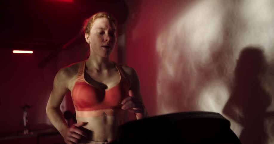 Woman with ponytail orange sports bra and black shorts runs on treadmill at the gym