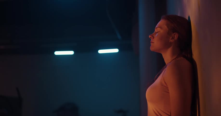 A woman is standing against a wall breathing heavily and she walks away