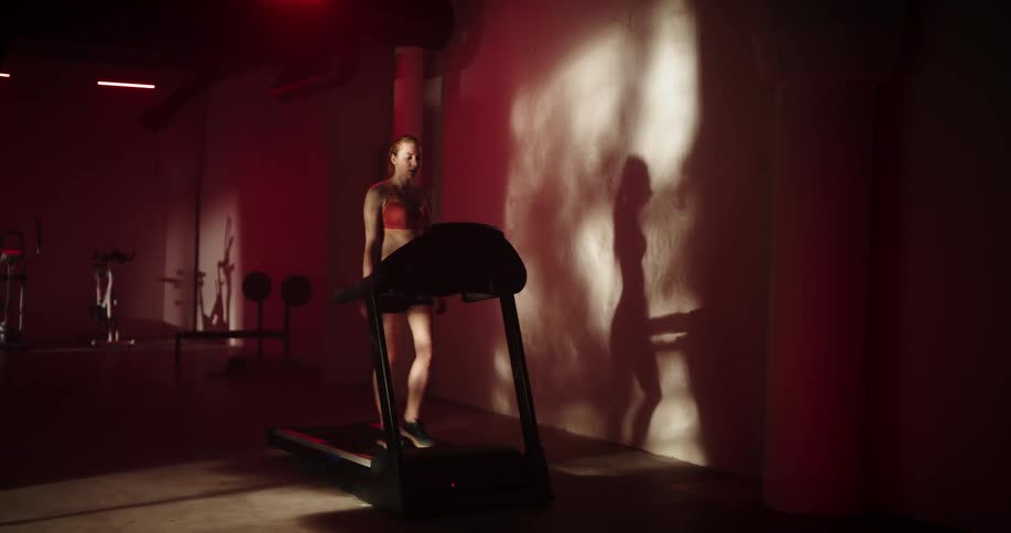Woman with ponytail orange sports bra and black shorts walks on treadmill at the gym