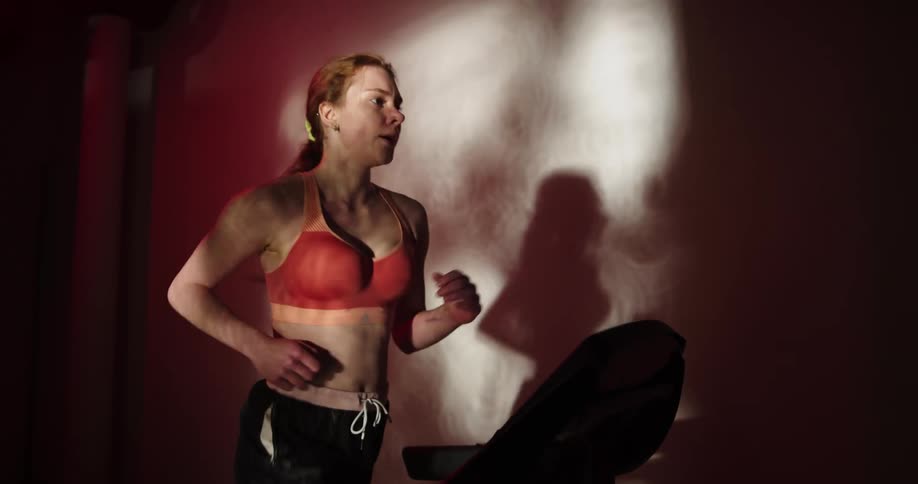 Woman with ponytail orange sports bra and black shorts exercises on treadmill in the gym