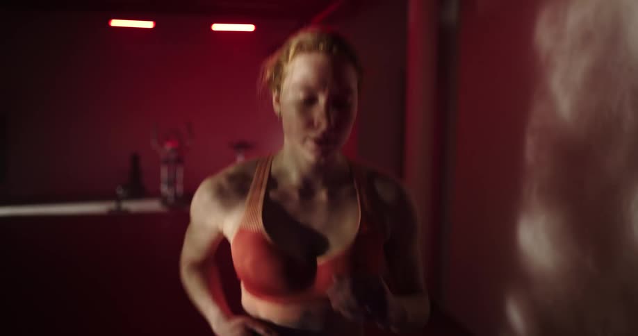 Woman with ponytail and orange sports bra jogs on treadmill at the gym