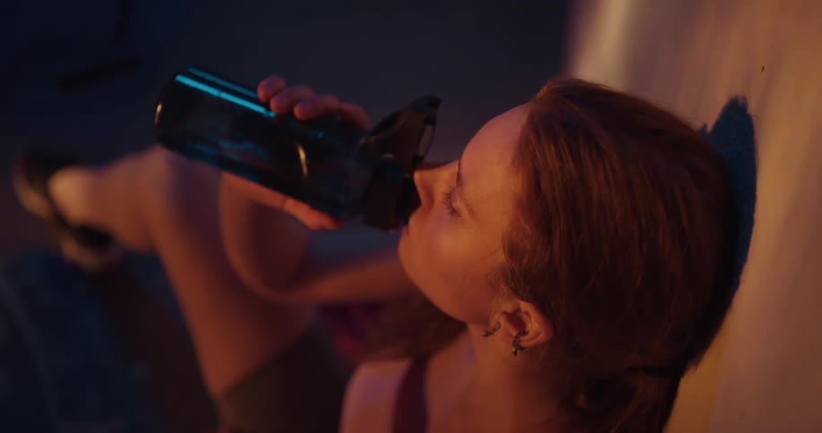 A woman taking a break at a gym to drink from a bottle of water