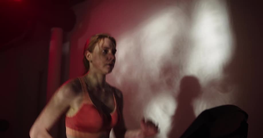 Woman with ponytail and orange sports bra runs on treadmill at the gym