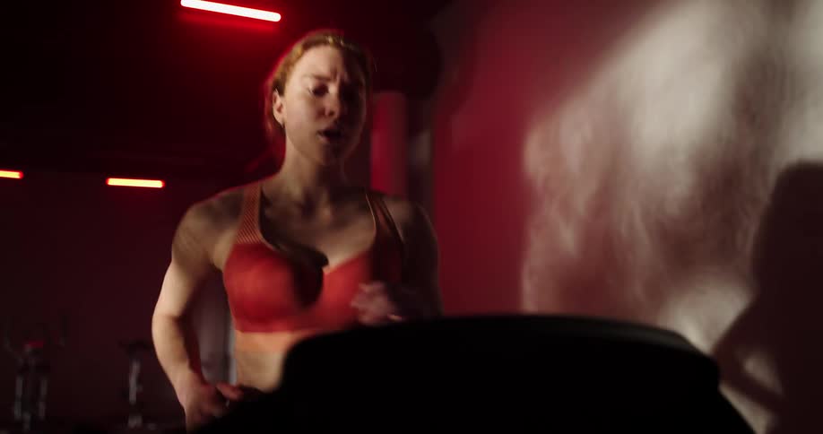 Woman with ponytail and orange sports bra runs on treadmill in a gym
