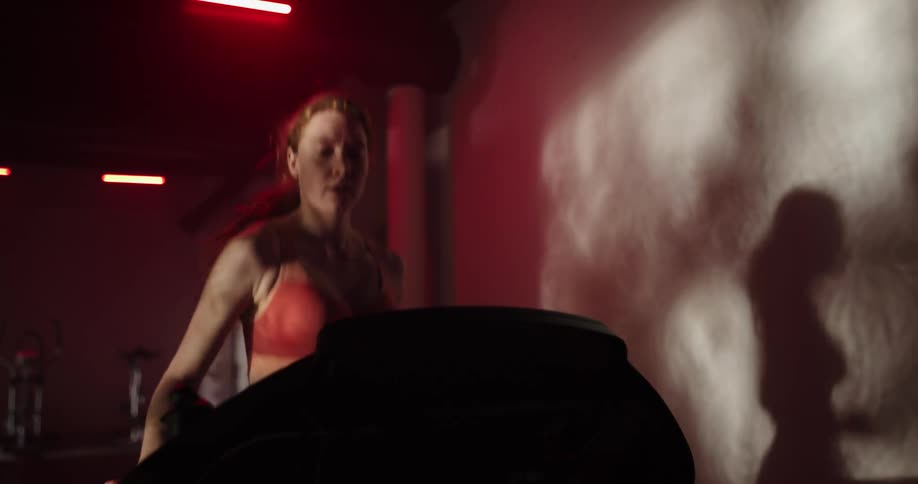 A woman smiles as she runs on a treadmill and her shadow moves on the wall