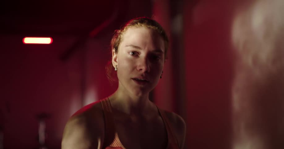 Woman with ponytail sports bra and black shorts walks on treadmill smiling at camera at the gym