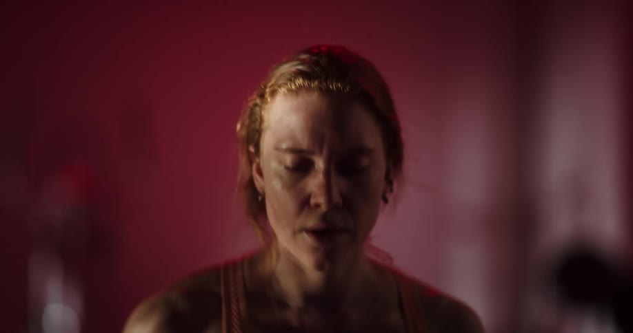 Red haired woman runs on treadmill in dimly lit room