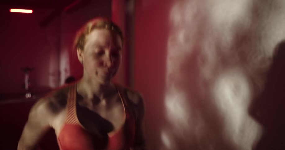 Woman with ponytail and orange sports bra runs on treadmill in a gym