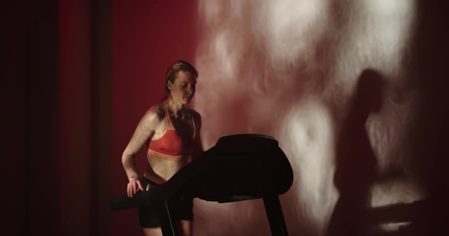 Woman with ponytail orange sports bra and black shorts runs on treadmill at the gym