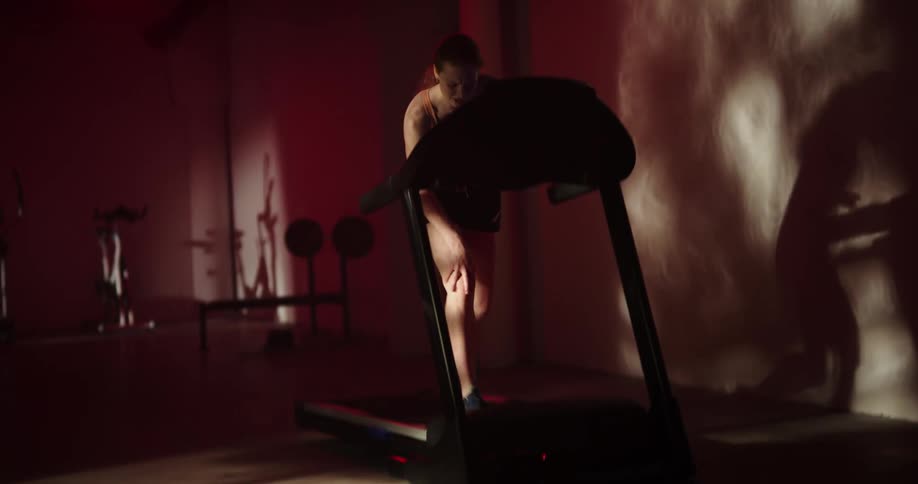 A woman running on a treadmill suddenly hops off holding her knee