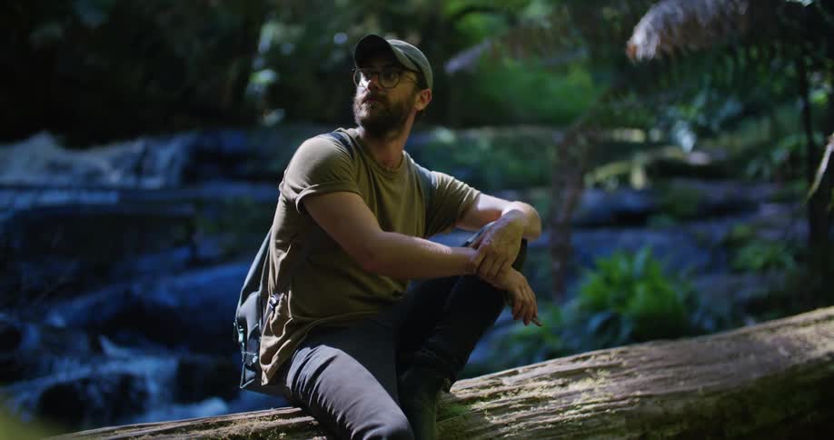 Man looks around while sitting near river with short waterfalls