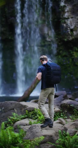 Blonde hiker climbs over boulders near waterfall