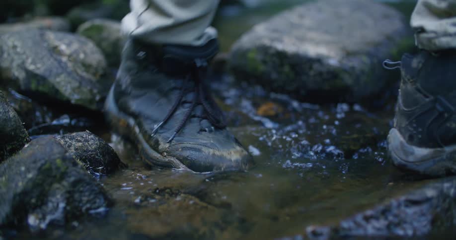 A person in hiking boots stepping in a stream