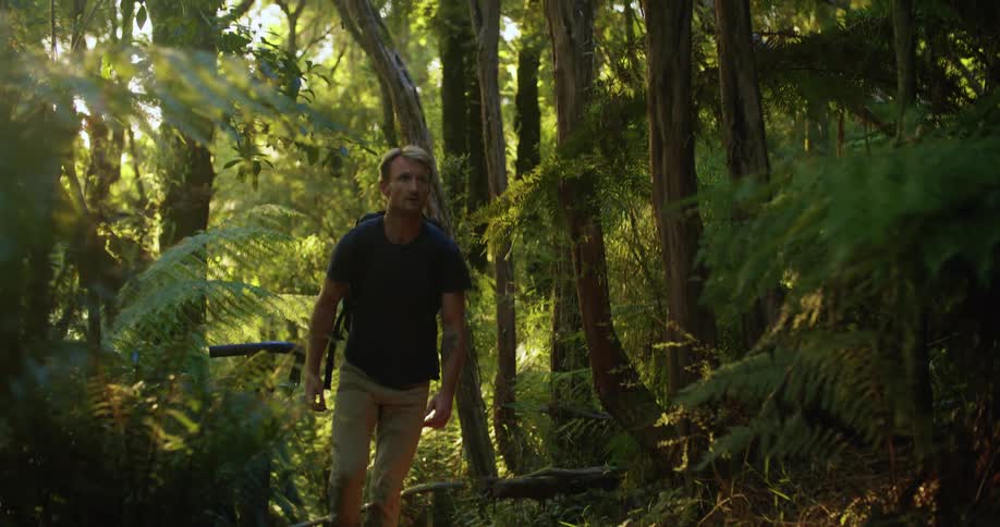 A man wearing a backpack is walking on a trail in the woods