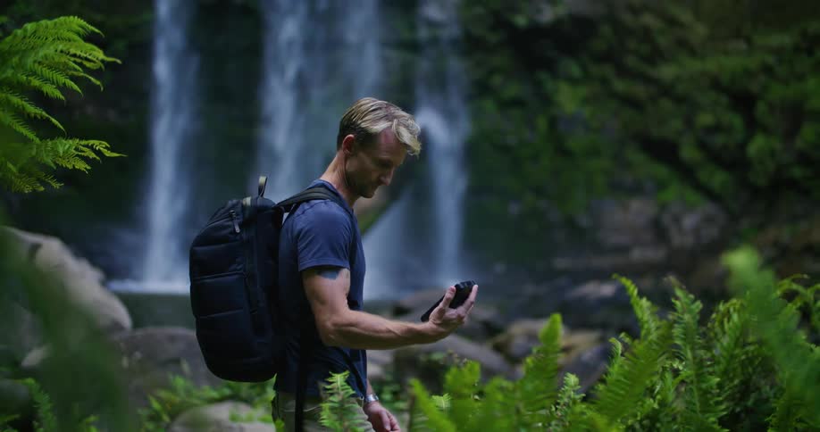 A man wearing a backpack hiking near a waterfall in nature