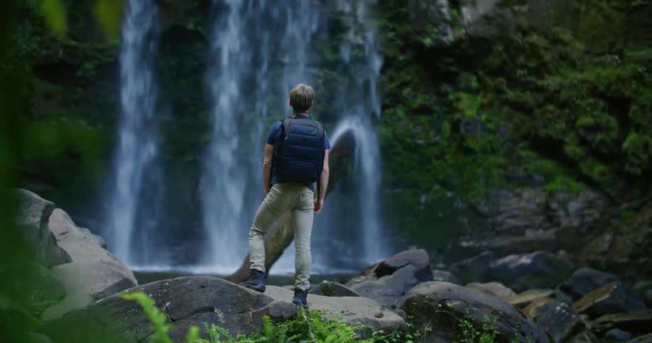 A man is hiking past the waterfall