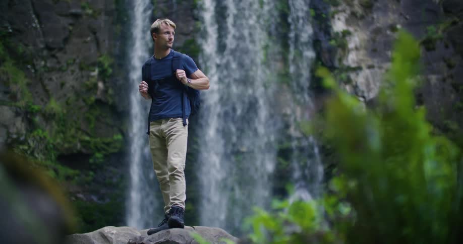 A male hiker standing in front of a waterfall in nature