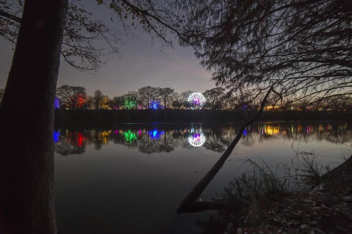 Carnival lights are seen beyond a lake as day dusk turns to night