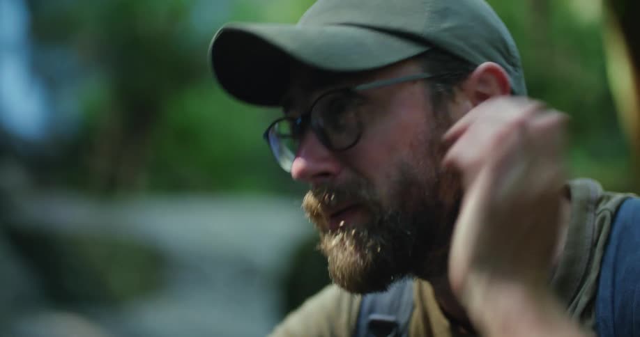 A man is resting in a wooded area and wearing a hat