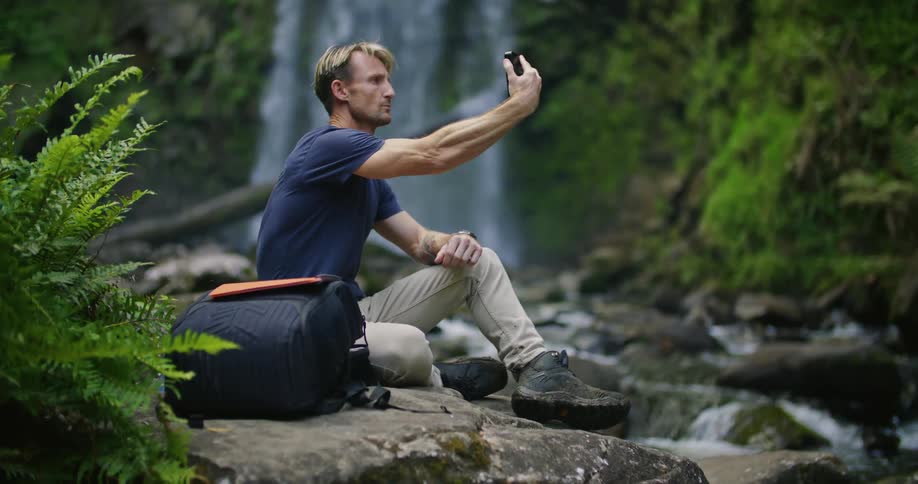 A man is using his cell phone by the waterfall