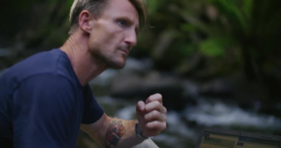 A man is looking at a map on his laptop near the stream